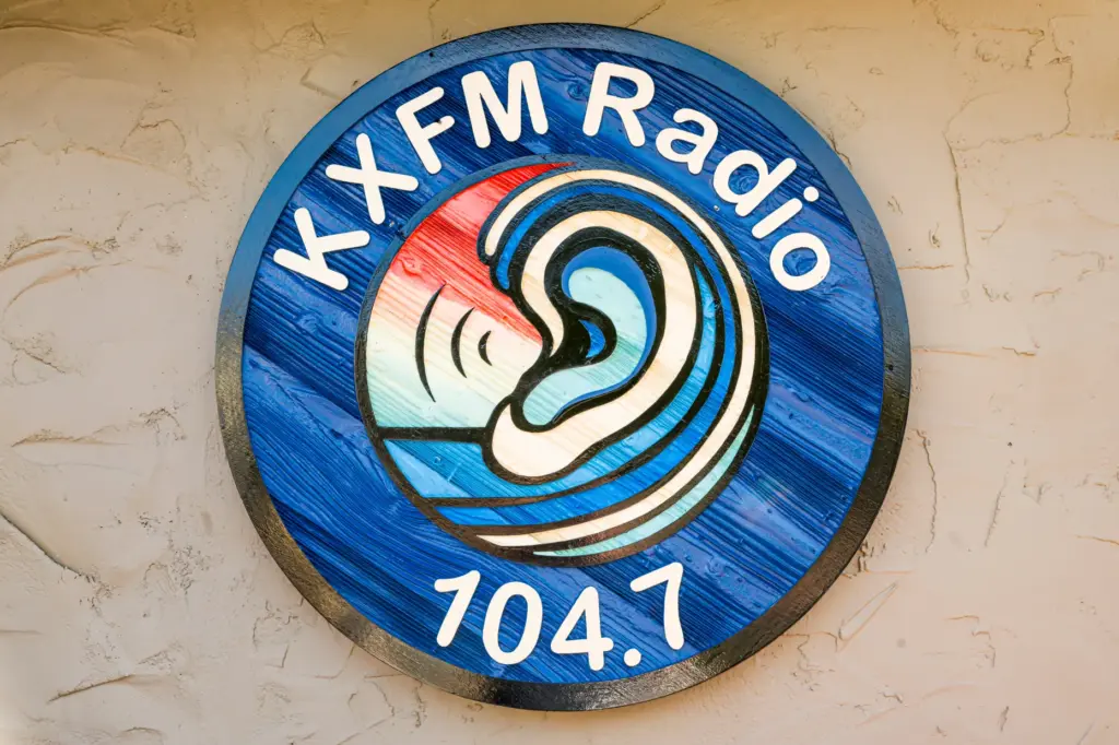 The KXFM Radio 104.7 logo hangs on the outside of...