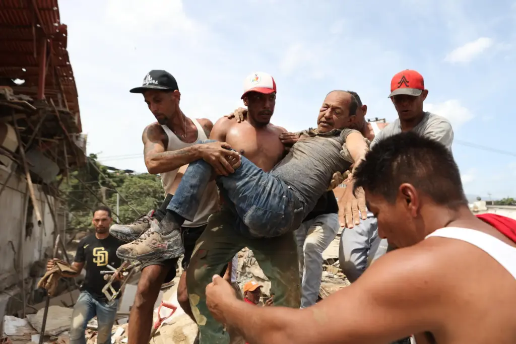 Neighbors carry a man rescued from the rubble of a...