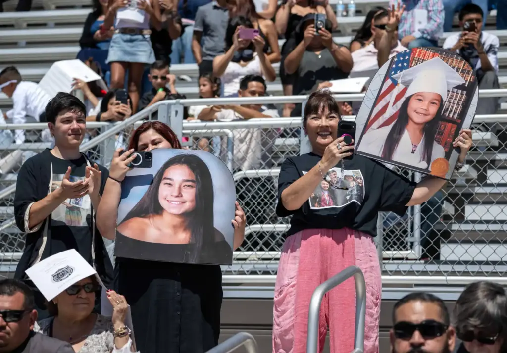 Proud parents hold up enlarged photos of their kids as...