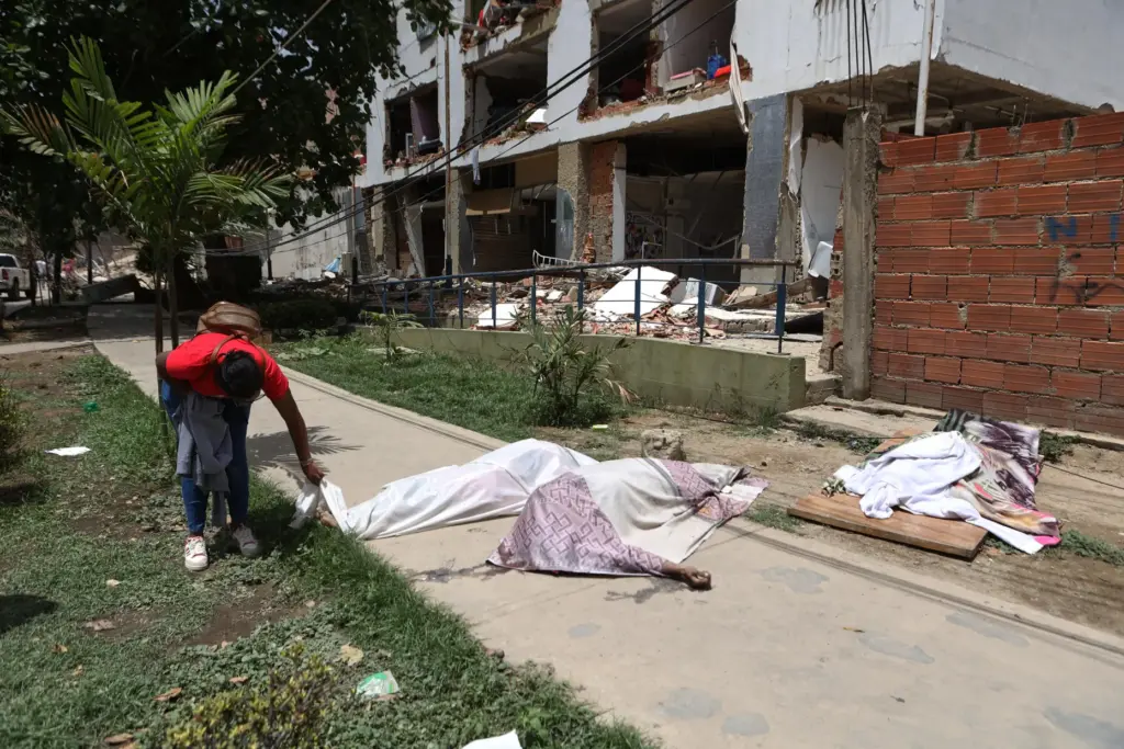 A man looks at covered bodies in front of a...