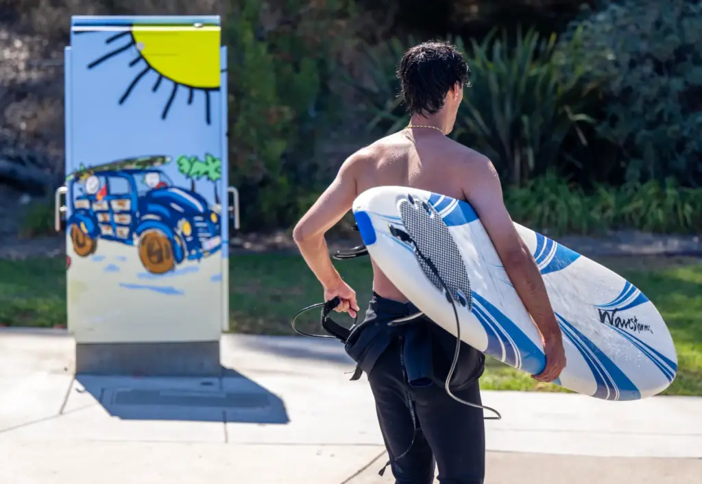 A surfer walks past a painted utility box, entitled âBeach...