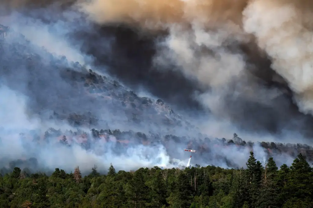 A helicopter provides bucket drops to assist firefighters battling the...