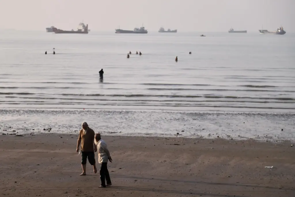 Men walk on the shoreline as people wade in the water in the Strait of Hormuz.