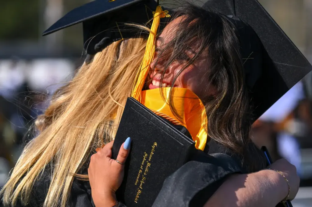 Graduate Maya Aoude, right, hugs a classmate after getting their...