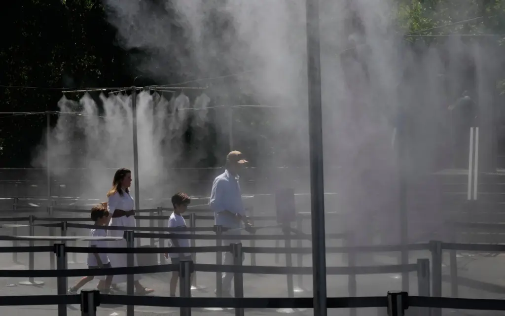 A family walks through a cooling water spray at the...