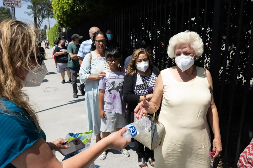 From left, volunteer Lorena Bautista hands Rosa Chambers a bottle...