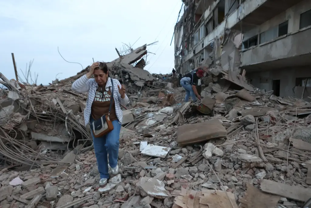 Residents walk among the rubble of building damaged in an...