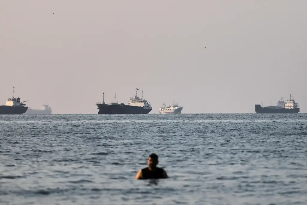 A person stands on shallow water as cargo and commercial...