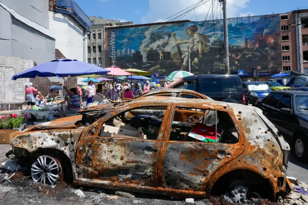 People buy food at an improvised outdoor market, burnt cars...