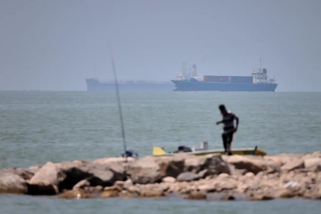 A man stands beside a fishing pole along the shore...
