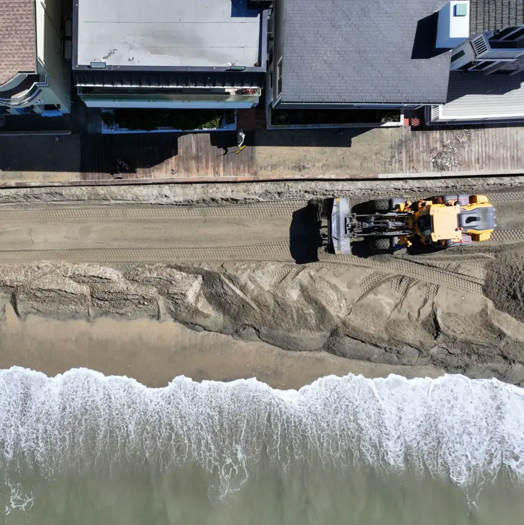 Ken Holt cleans up sand along the boardwalk in front...