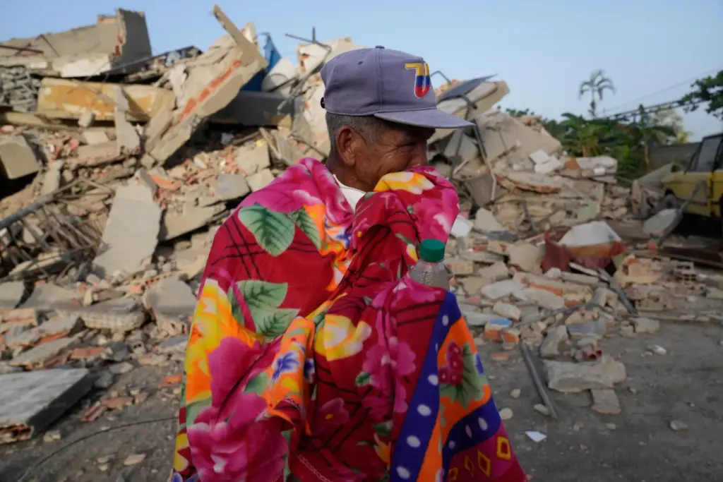 A man stands in front of a collapsed building two...