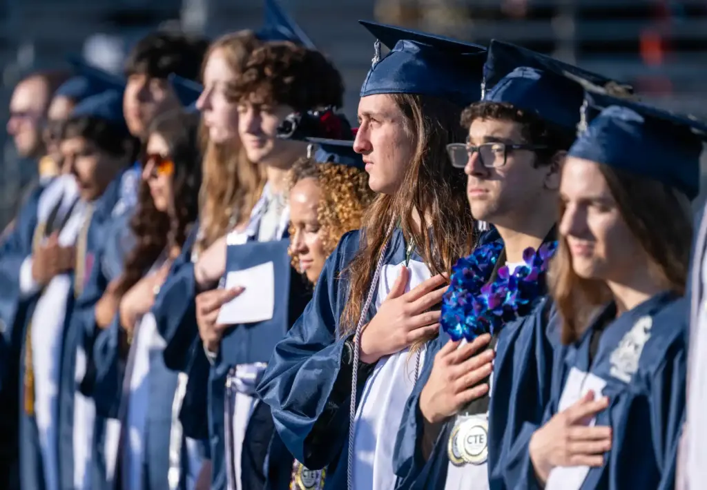 Graduates stand and cover their hearts for the national anthem...