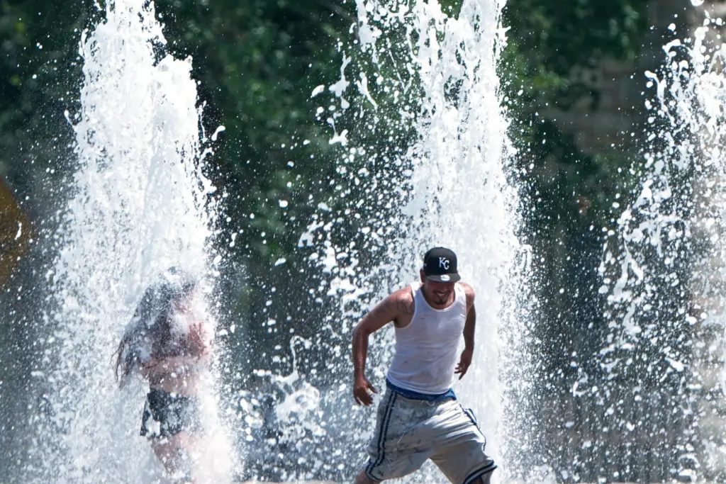 People cool off in a fountain during hot weather Monday,...