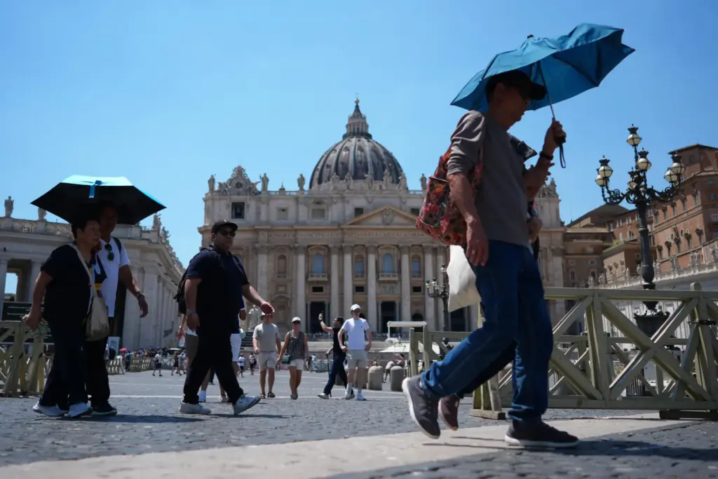 People shade from the sun under umbrellas as they walk...