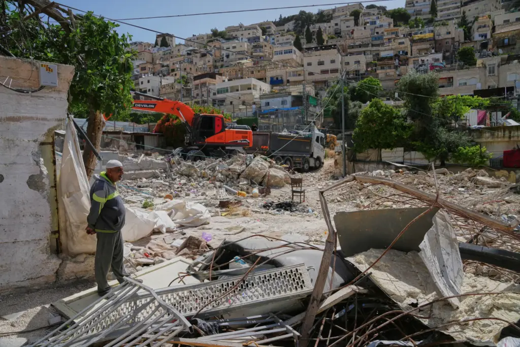 A Palestinian man looks on as an excavator clears the rubble of demolished homes.