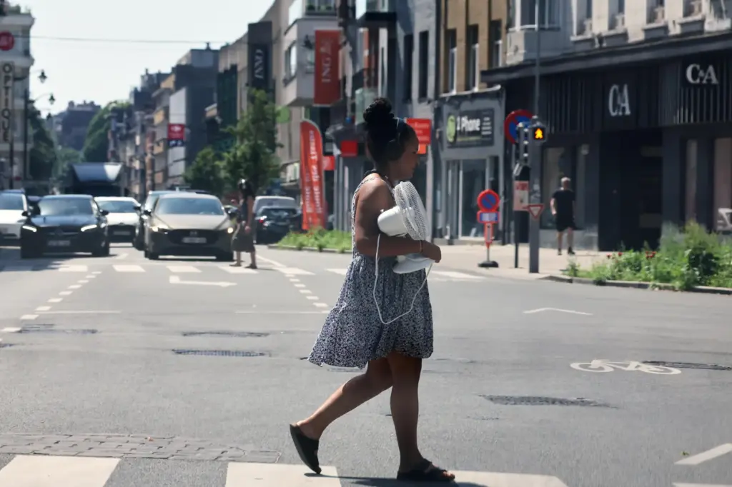 A woman walks across the street with a fan in...