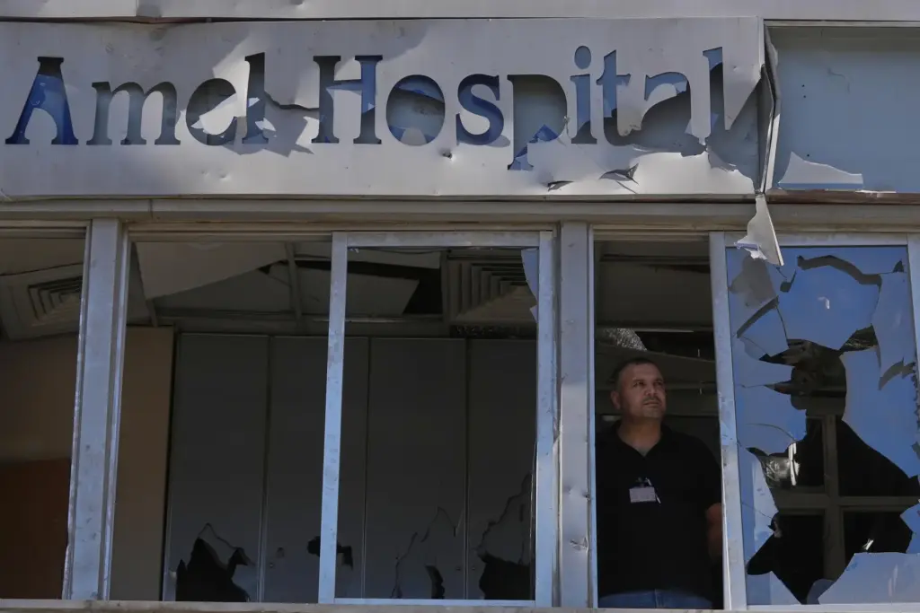 A man stands behind shattered windows at Jabal Amel Hospital,...