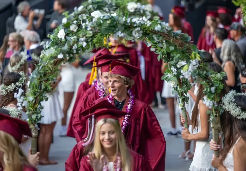 Laguna Beach High School grads walk through flower arches as...