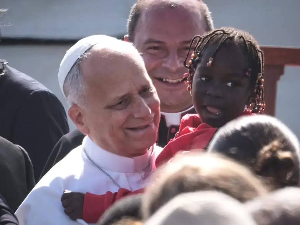 Pope Leo XIV holds a young assistant as he arrives for a meeting with migrants.