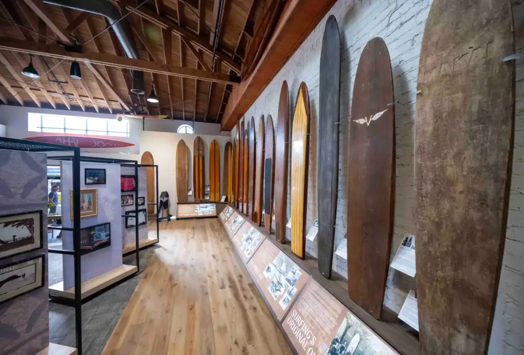 A collection of antique surfboards, mostly made of wood, hang...
