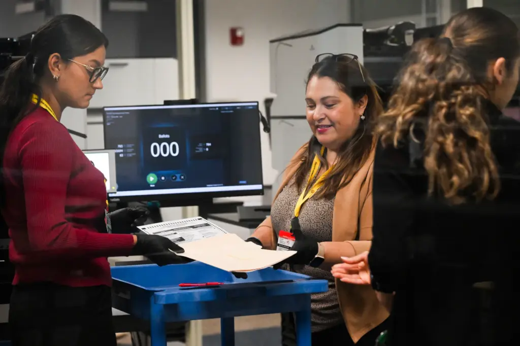 Temporary election assistants monitor and count ballots as they pass...