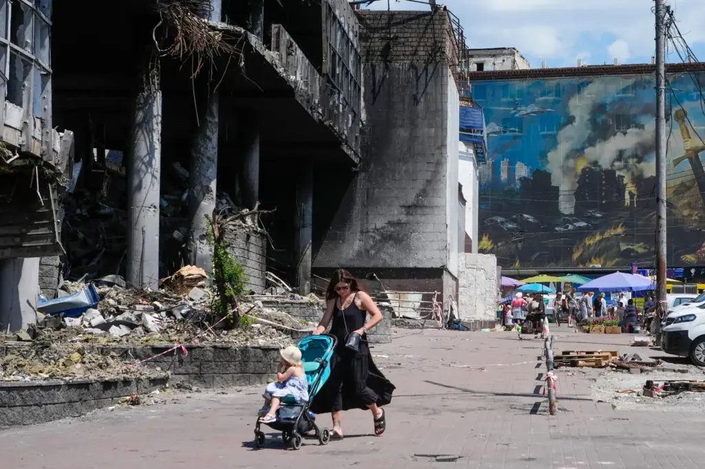 A mother pushes a stroller past a damaged building covered...