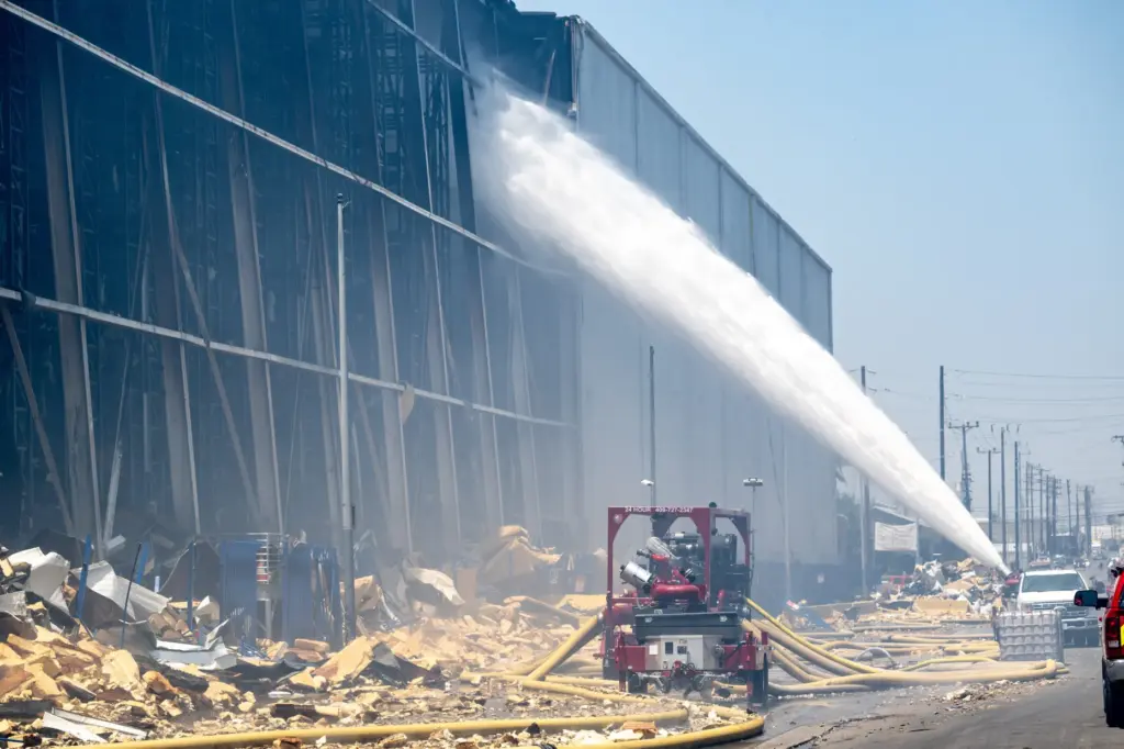 Firefighters use a high-powered water canon from Texes to douse...
