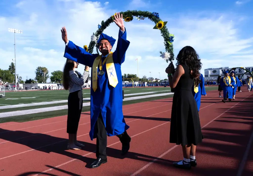 A graduate waves to the crowd in the stands in...