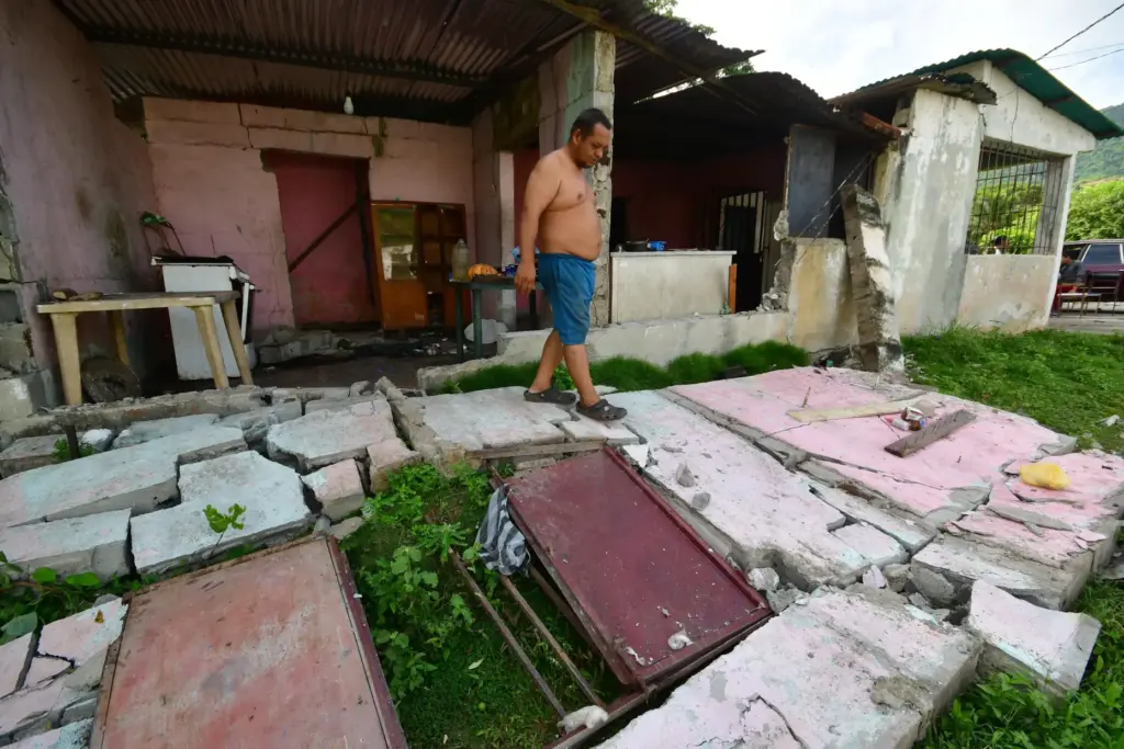 A man walks over the fallen walls of his home...