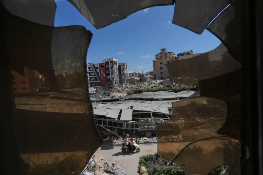 Buildings damaged by Israeli strikes are seen through shattered glass...