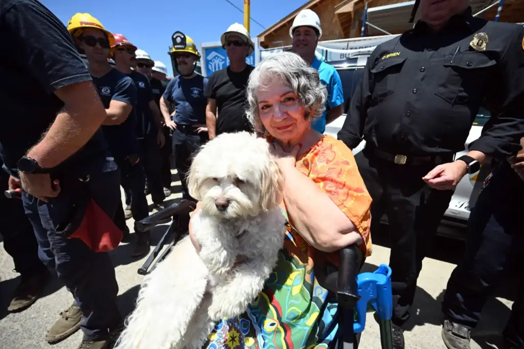 Rosa Fernandez holds her dog, Donut, surrounded by firefighters and...