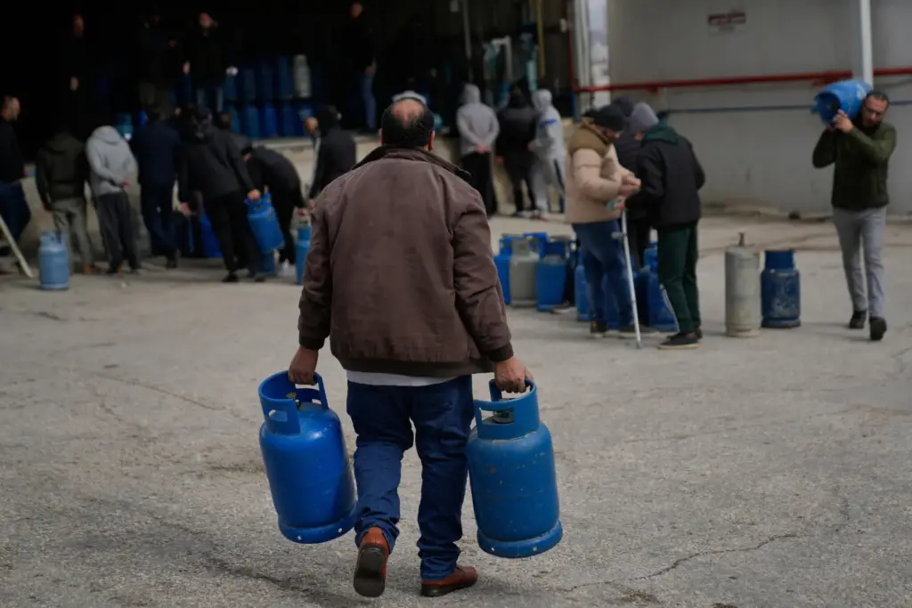 FILE – A Palestinian man carries his empty cooking gas...