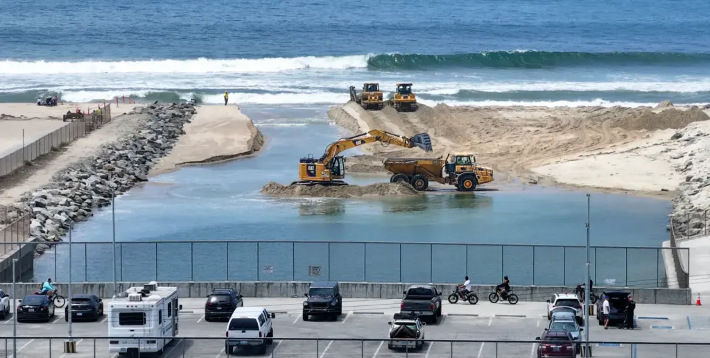 Workers clear sand from the opening between the Talbert Marsh...