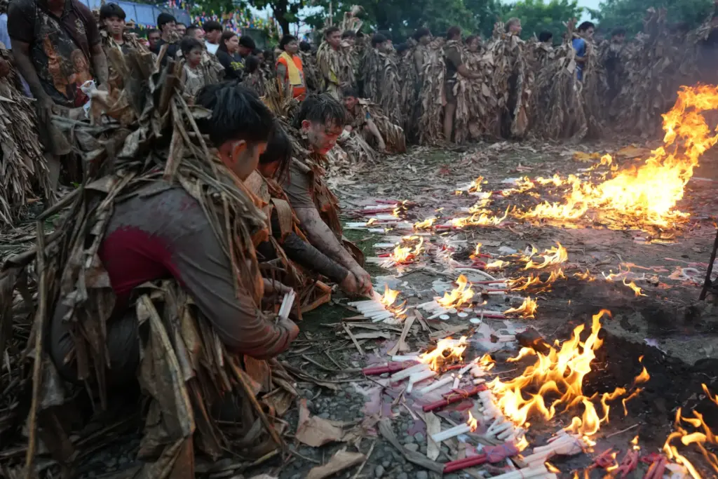 Catholic devotees covered in mud and dried banana leaves light...
