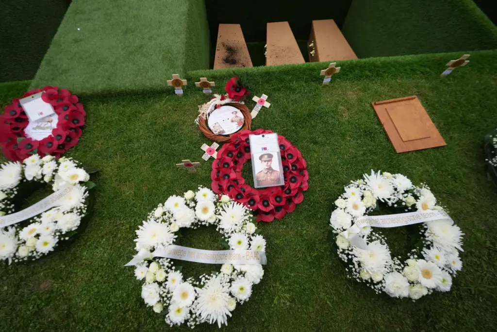 Poppy wreaths and photos stand beside the graves during a...