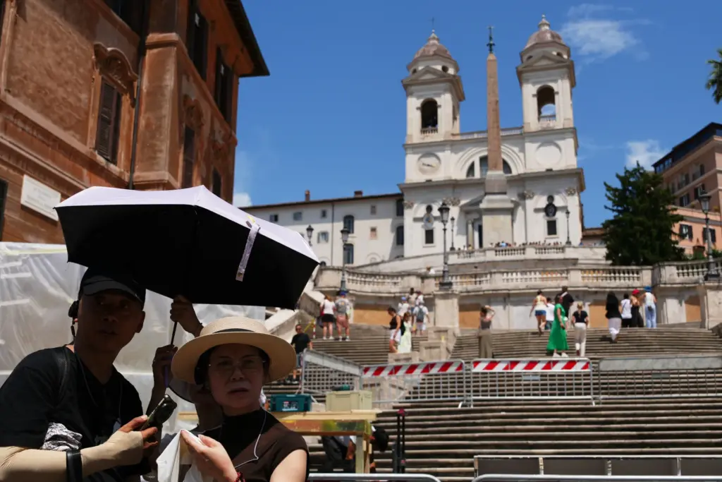 Tourists use umbrellas to shelter from the sun as they...