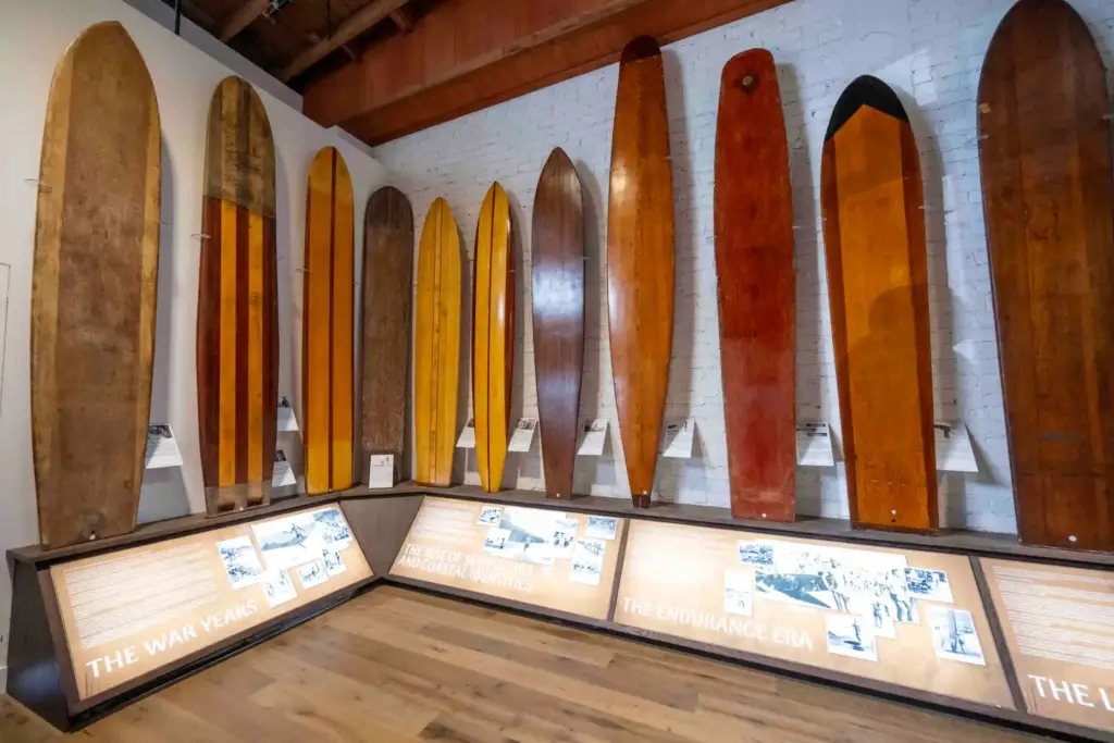 A collection of antique surfboards, mostly made of wood, hang...
