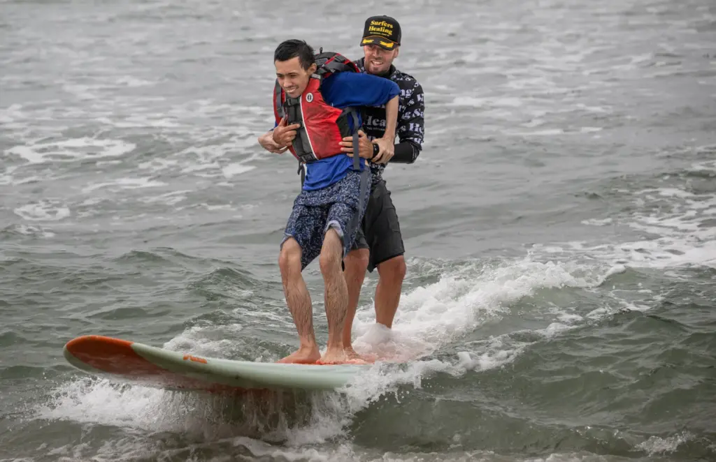 Gene Fernando, 33, left, gets assistance from Surfers Healing volunteer,...