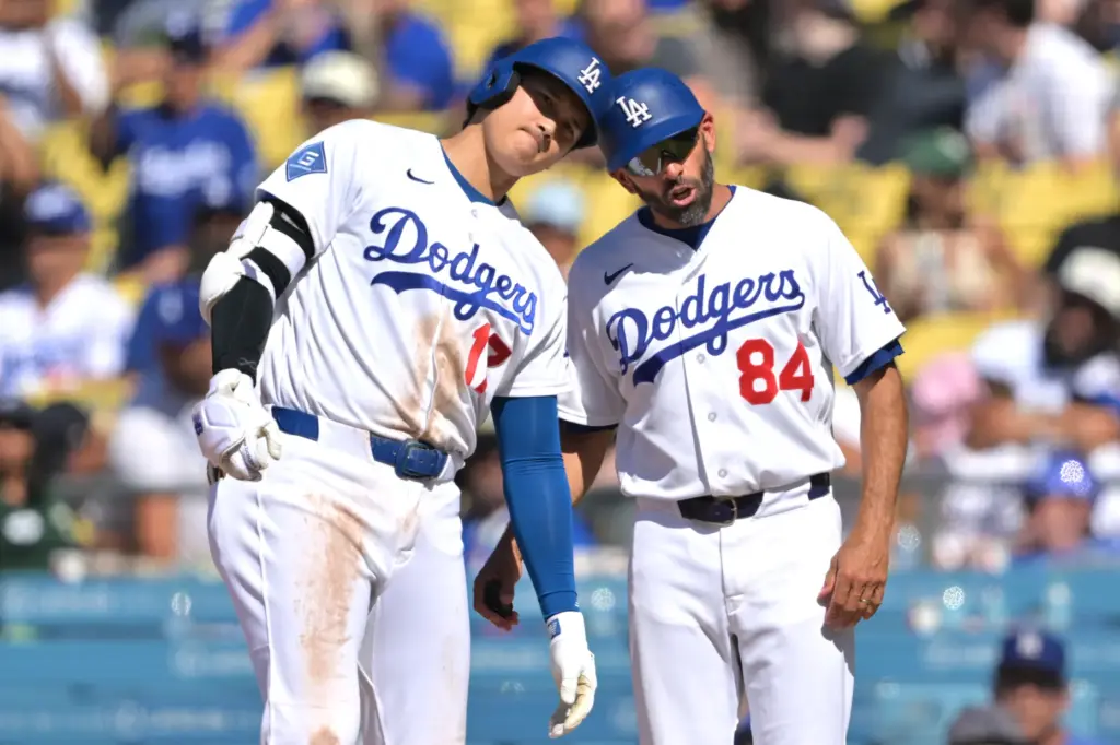 Dodgers’ Shohei Ohtani taps helmets with Dodgers’ first base coach...