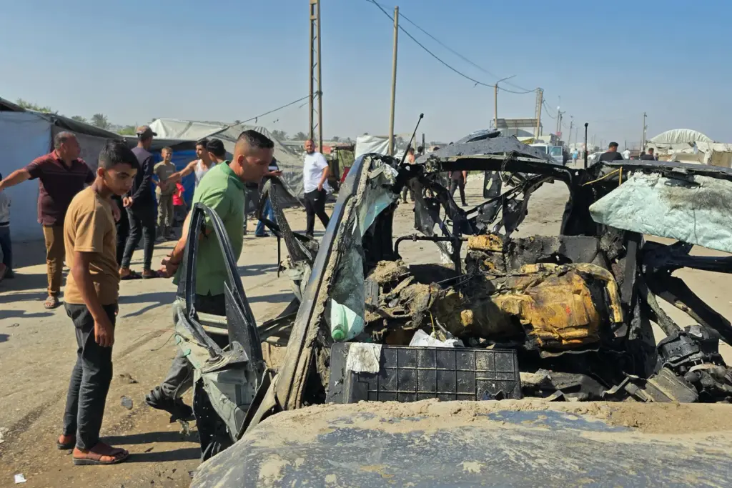 Palestinians look at a destroyed car following an Israeli military strike.