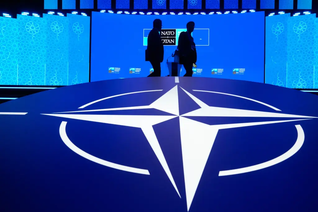 Two men walk past the NATO logo.