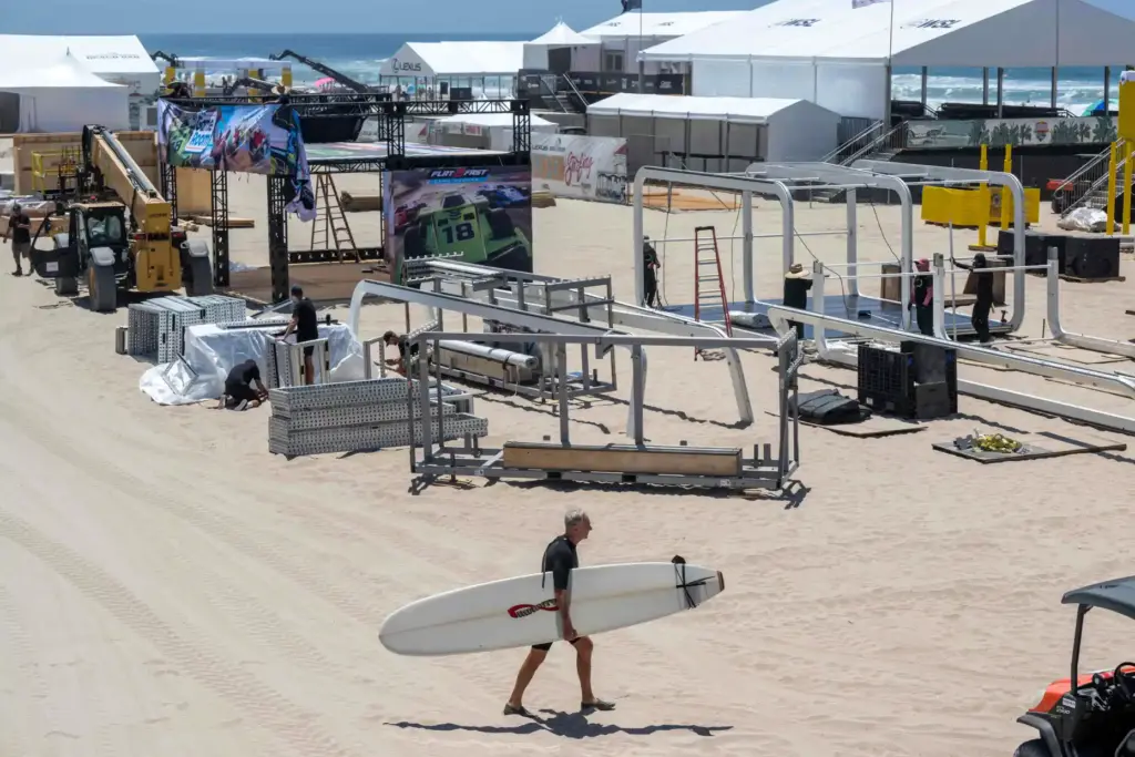 A surfer walks towards the water as workers construct the...