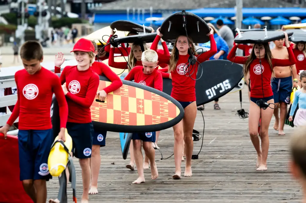 San Clemente junior lifeguards walk with their surfboards and body...