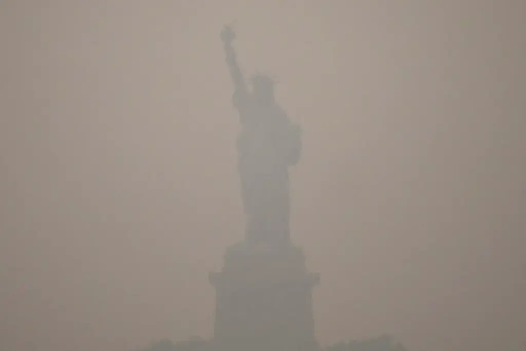 The Statue of Liberty stands during sunset as smoke from wildfires blankets the sky.
