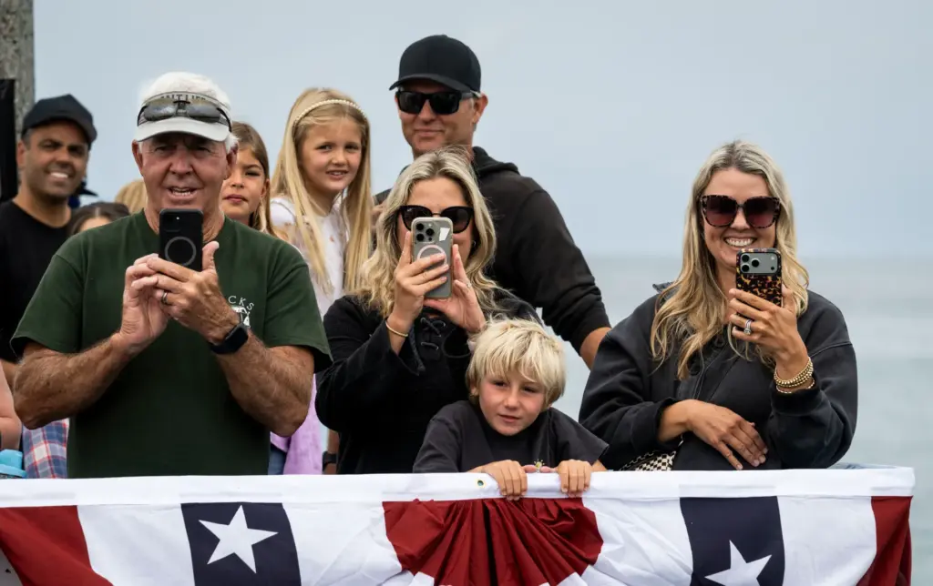 Supporters take photos as their junior lifeguards jump off the...