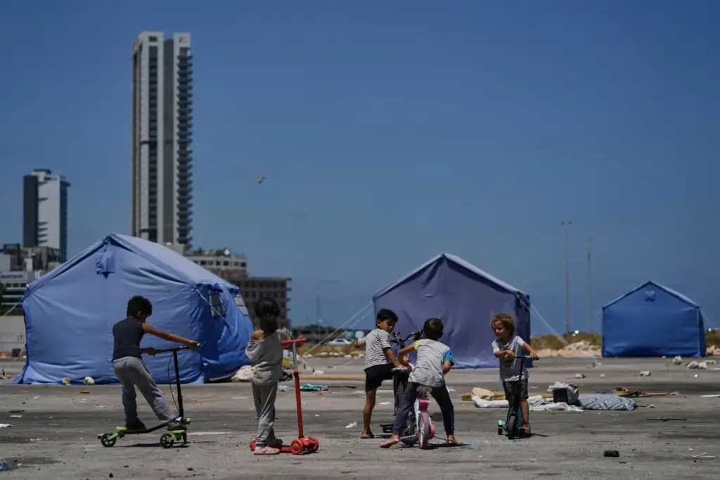 Children play outside their family’s tents, used as shelter after...