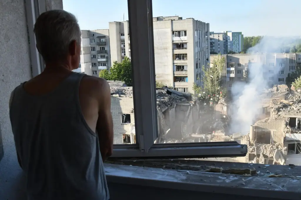 A man watches as rescuers clear the rubble at a damaged apartment building.
