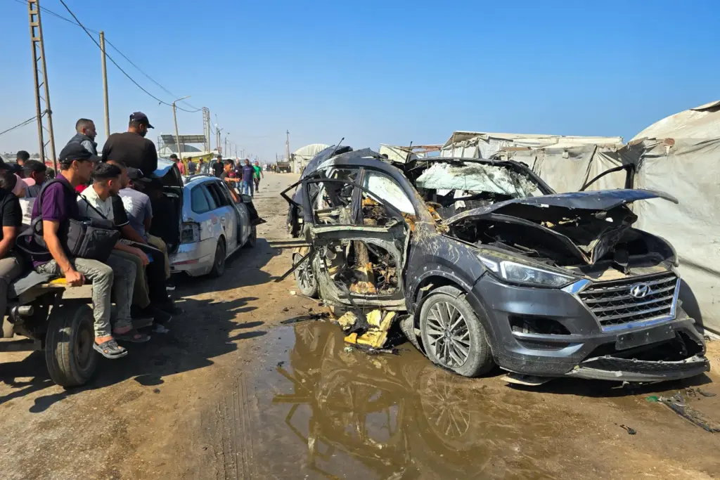 Palestinians look at a destroyed car following an Israeli military strike.