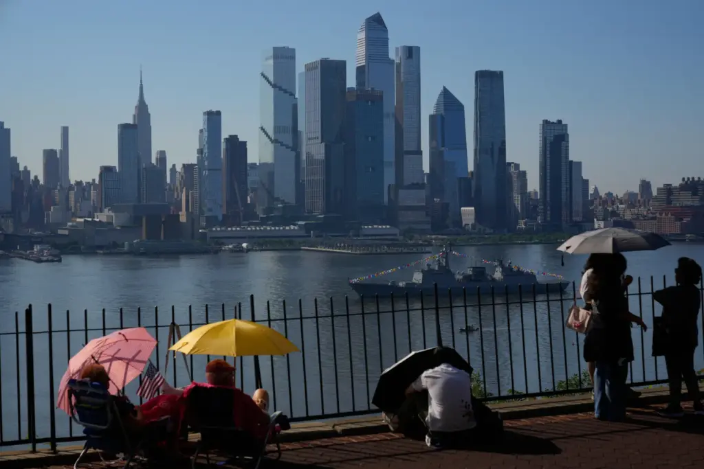People take cover from the heat under umbrellas as they...